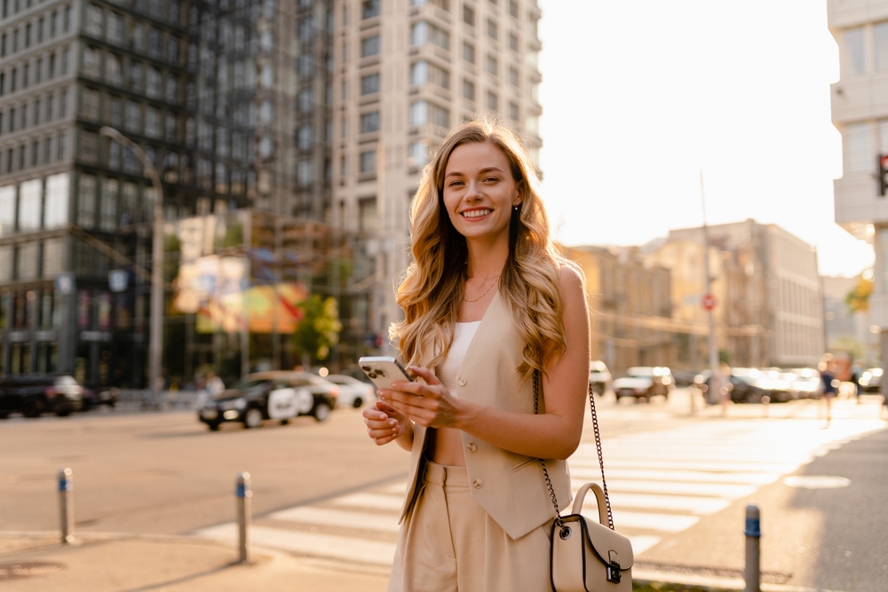 Pretty,Blonde,Woman,Walking,In,Sunny,City,Street,With,Phone,